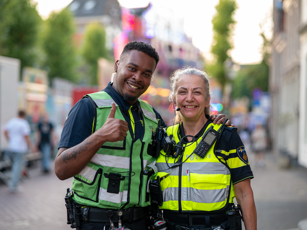 Medewerker van de evenementenhulpverlening en politieagent poseren samen tijdens een druk evenement in de stad.