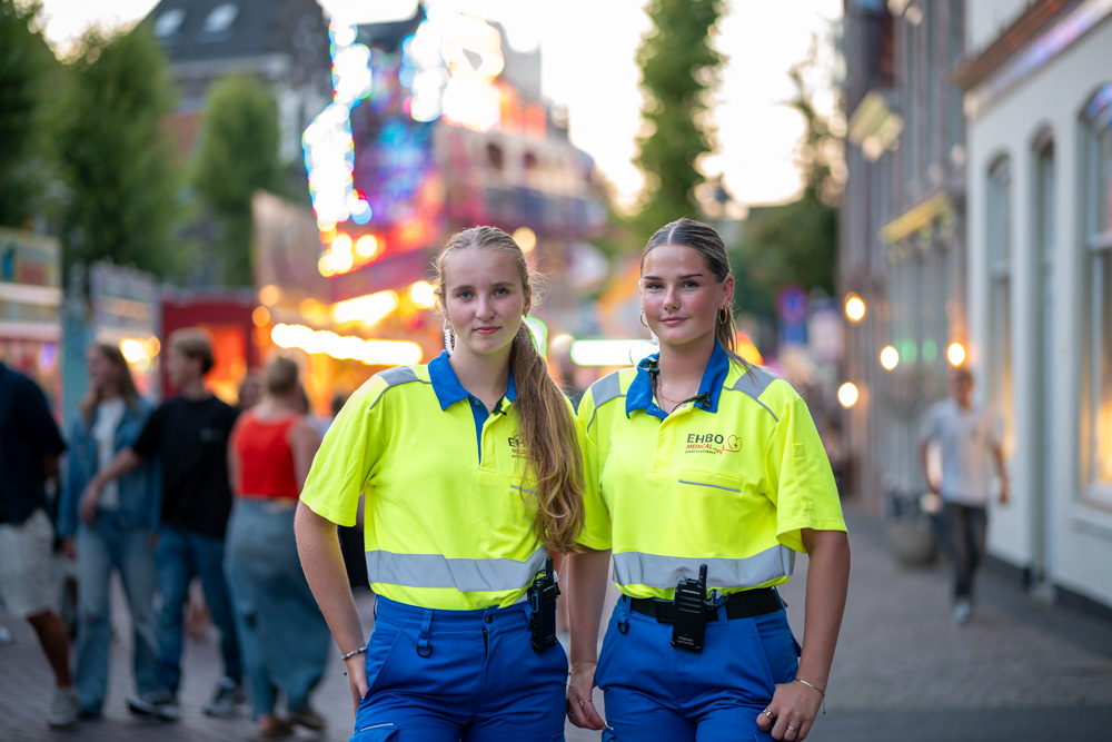 Twee EHBO-medewerkers in reflecterende werkkleding tijdens een druk evenement in de stad.