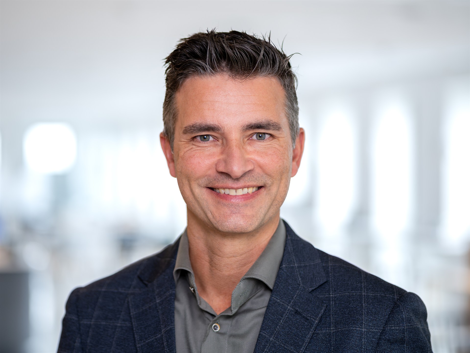 Zakelijk portret van een glimlachende mannelijke professional in een lichte kantooromgeving.