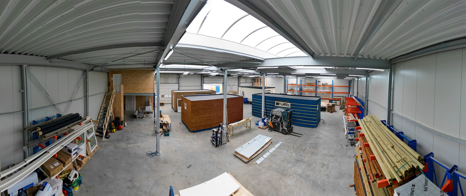 Overzicht van de productiehal van Prefab Care met prefab zorgunits, bouwmaterialen en machines.