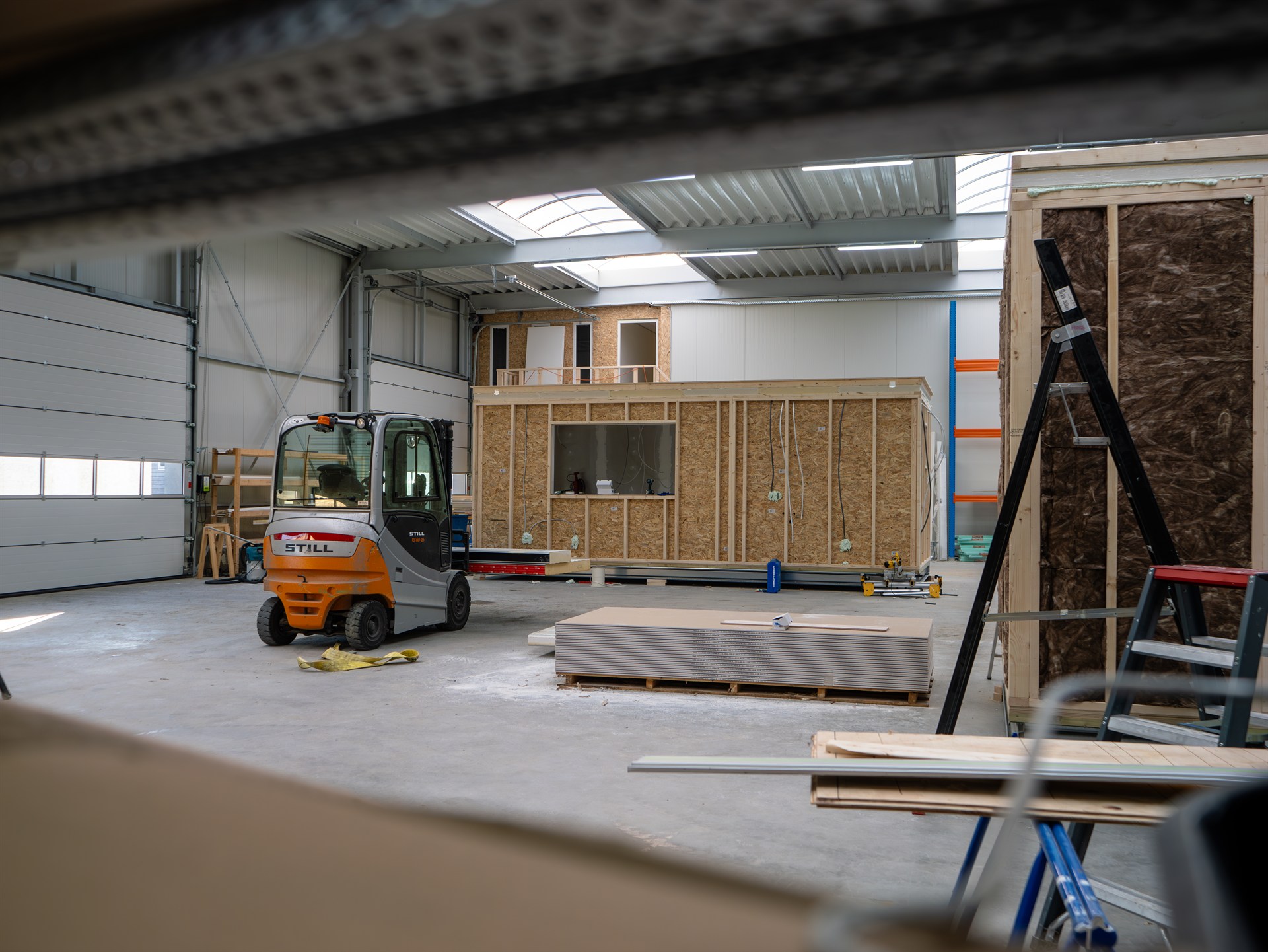 Prefab zorgunit in aanbouw in de werkplaats van Prefab Care, met heftruck en bouwmaterialen.