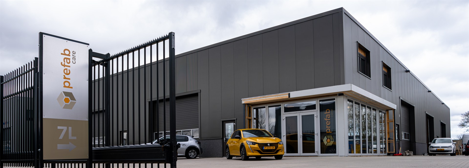 Buitenzijde van het bedrijfspand van Prefab Care met bedrijfslogo en gele auto voor de ingang.